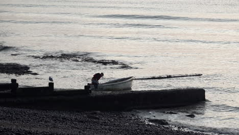 A-fisherman-pushes-his-boat-out-to-sea-and-uses-oars-to-row-out-over-small-waves-rolling-in-on-the-shore-at-dawn