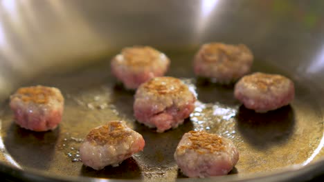 Small-size-juicy-meat-balls-frying-in-a-steel-pan,-handheld-close-up-shot