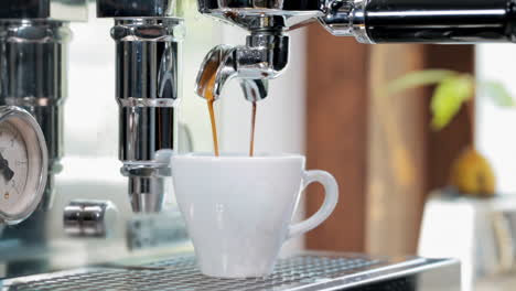 Nahaufnahme-Einer-Weißen-Espressotasse,-Die-über-Köstlichen-Goldbraunen-Kaffee-Gießt,-Der-Aus-Leckeren-Kaffeebohnen-In-Der-Espressomaschine-Gewonnen-Wird