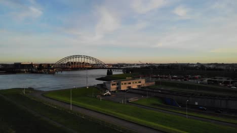 Drone-pan-shot-of-vehicles-driving-into-a-tunnel-underneath-a-river-while-cars-driving-on-a-bridge-above-the-water-on-a-partly-cloudy-day-during-golden-hour-on-a-winter-day-in-the-netherlands