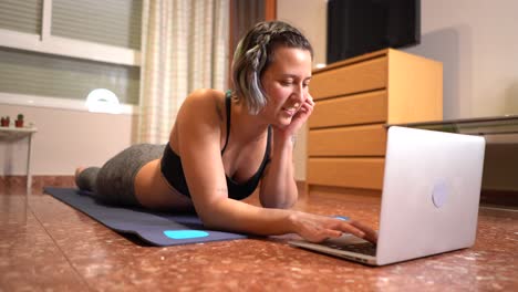Woman-smiles-stretched-out-on-the-mat-operating-the-computer-ready-to-play-sports
