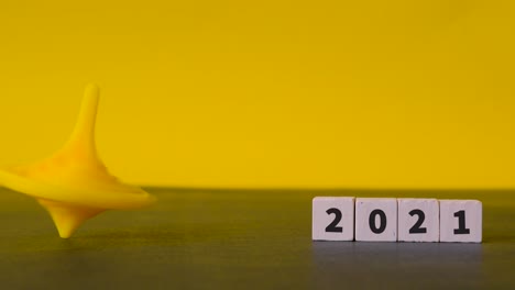 Eine-Menschliche-Hand-Dreht-Einen-Gelben-Kreisel,-Der-Wackelt-Und-Ordentlich-Neben-Holzklötzen-Mit-Den-Zahlen-2021-Darauf-Liegt