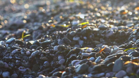 Close-up-of-shiny-pebbles-at-Kalamata-beach,-tilt-reveal-blurry-waves-slow-motion-120fps