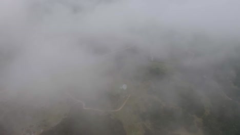 Aerial-flight-through-clouds-and-abandoned-bivouac-standing-on-mountain-in-green-terrain-area