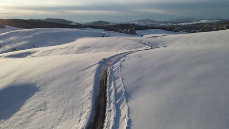 Aerial-shot-of-hills-covered-with-snow-and-a-car-passing-through-a-road-in-the-middle-of-snowy-valley