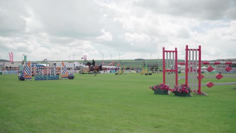 Equestrian-Competition-At-An-Agricultural-Show---Rider-On-Horse-Jumping-High-On-The-Obstacle-Bars-In-Cornwall,-England,-UK