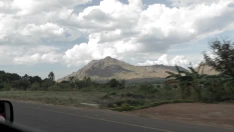 Highway-travel-in-Malawi-Africa-with-farms,-mountains,-and-vehicles-seen,-View-from-vehicle-advancing
