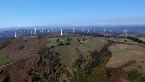 Wind-farm-with-wind-turbines-moving-the-helices-in-the-mountains-with-forests-of-green-trees-on-a-sunny-afternoon