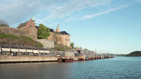 Ein-Zeitraffer-Mit-Panoramablick-Auf-Den-Fjord-In-Oslo-Mit-Einer-Burg-Im-Hintergrund-Vor-Einem-Blauen-Hügel