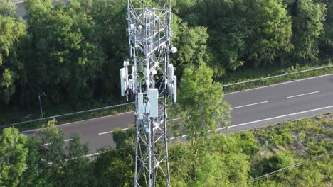 5G-broadcasting-tower-antenna-in-British-countryside-with-vehicles-travelling-on-highway-background-aerial-orbit-view-left