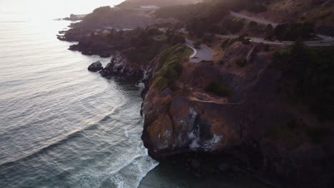 Drone-shot-of-waves-crashing-onto-the-jagged-cliffs-at-Yaquina-Point-in-Newport,-Oregon-during-sunset