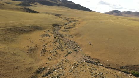 Three-horse-riders-on-plain-in-Mongolia,-aerial-pan
