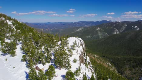 Aerial-Shot-Of-Large-Snow-Covered-Rocky-Cliff-Hanging-Over-Wide-Open-Lush-Green-Alpine-Forest-Mountain-Valley-In-Rocky-Mountains-Mount-Evans-Colorado-USA