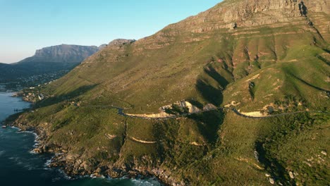 Chapmans-Peak-road-coastline-during-sunset-with-table-mountain-in-background,-aerial