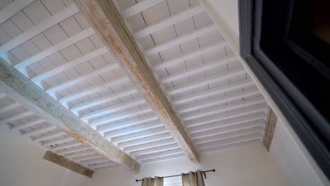 Wood-beam-vintage-ceiling-with-chipped-paint-at-rustic-villa-in-Southern-France,-Looking-up-pan-right-shot