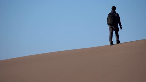 Man-hiking-over-sand-dunes-on-a-sunny-day