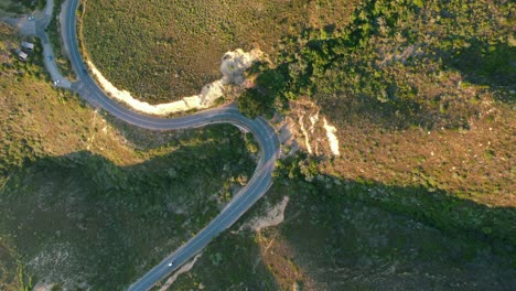 car-driving-on-Chapmans-Peak-Road-on-coast-of-Cape-Town-at-sunset,-top-down-aerial