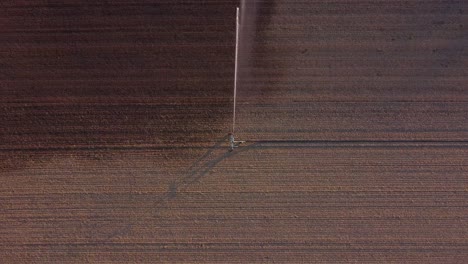 Aerial-Top-Down-View-of-irrigation-and-Watering-Machinery-in-the-Middle-of-Agricultural-Farmland,-Water-Splashing-Around-on-Soil