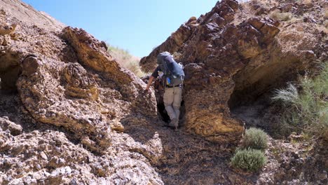 Erwachsener-Männlicher-Wanderer-Klettert-Vorsichtig-Mit-Großem-Rucksack-Auf-Dem-Ramon-Krater-Trail-In-Israel-Auf-Eine-Kleine-Felswand