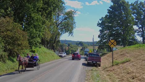 An-Amish-Horse-and-Open-Buggy-Approaching-Down-a-Country-Road-Passing-Cars,-With-Amish-Teens,-on-a-Beautiful-Sunny-Day