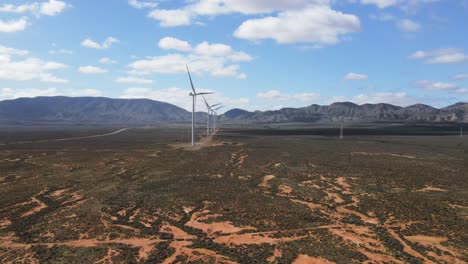 Drone-aerial-moving-towards-renewable-energy-wind-farm-in-country-desert-Australia-with-mountains-in-the-background-on-a-summer-day