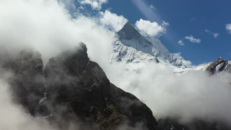 Aerial-drone-shot-going-around-clouds-to-reveal-snow-topped-mountain-in-the-Annapurna-mountains,-Nepal