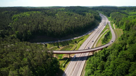 Drone-shot-of-traffic-on-polish-highway-with-modern-curvy-bridge-surrounded-by-green-trees-and-forest-in-sunlight---Gdynia,Poland