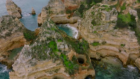 Pan-up-shot-from-the-Algarve's-rugged-coastline,-flying-through-the-rocks