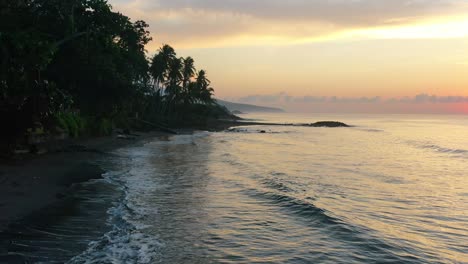 sun-rising-over-horizon-at-dawn-with-calm-ocean-waves-crashing-on-tropical-bali-beach,-aerial
