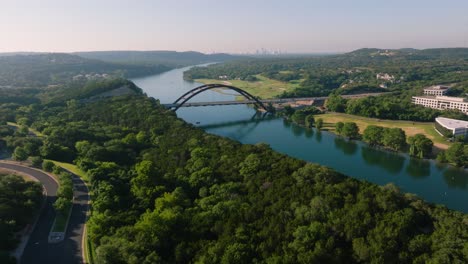 Aerial-sweep-of-the-iconic-Pennybacker-360-bridge-in-Austin,-Texas-during-hazy-summer-sunrise-morning-with-downtown-skyline-in-backdrop