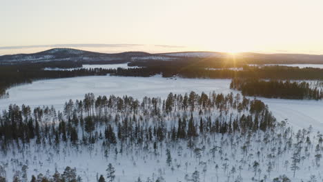 Snowy-freezing-Sweden-Lapland-quiet-snow-covered-woodland-scenery-aerial-view-orbiting-mountain-landscape-at-sunrise