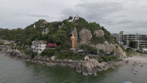 Drone-Flying-towards-Golden-Buddha-Statue-on-the-rocks-at-sea