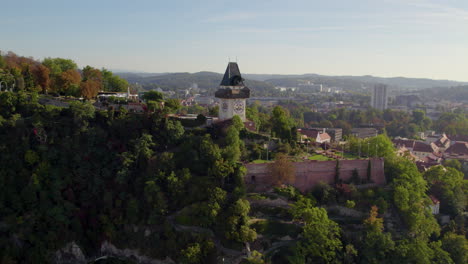 Aerial-view-across-Uhrturm-clock-tower-on-Graz's-Schloßberg-dolomite-woodland-hilltop-and-Graz-city-skyline