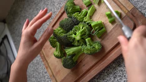Vertical-Shot-Of-Person-Chopping-Fresh-Green-Broccoli-In-Wooden-Board