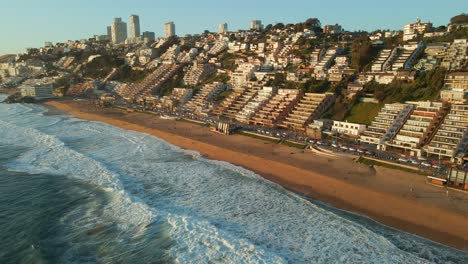 Aerial-view-flying-down-Reñaca-golden-cityscape-waterfront-with-sunny-scenic-tourism-beach-retreat