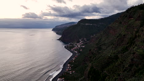 Sunset-aerial-along-rugged-Madeira-coastline,-small-coastal-village