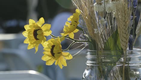 Close-up-of-a-mason-jar-of-flowers-on-a-table-at-an-outdoor-summer-wedding-reception