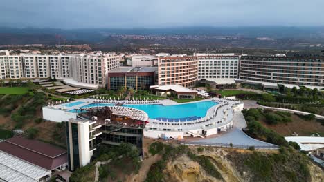Pan-shot-from-right-to-left-over-Elexus-Hotel-in-Nicosia,-Cyprus-with-a-big-pool-on-a-cloudy-day-with-hilly-terrain-in-the-background