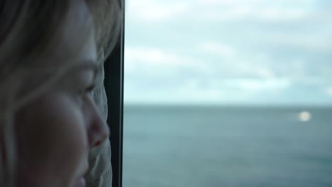 SLOWMO---Young-beautiful-blond-hair-woman-looking-out-of-window-with-ocean-view---CLOSE-UP