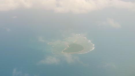 Bird's-eye-perspective-from-airplane-window-with-view-of-uninhabited-tropical-island-and-small-clouds