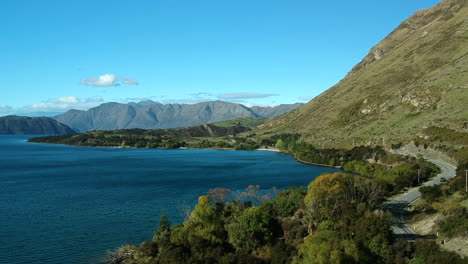 aerial-shot-of-Lake-Wanaka-with-a-car-drives-on-a-road-on-the-right-side