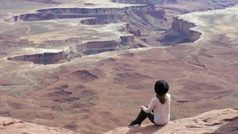 Slow-motion-shot-of-female-tourist-sitting-on-rock-enjoying-the-Island-in-the-Sky-in-Canyonlands-National-Park-in-Utah,-USA