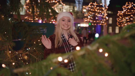 Young-woman-surprises-partner-by-popping-out-from-behind-Christmas-tree-and-smiling