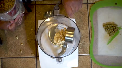 Pouring-cashew-nuts-into-a-food-processor,-View-from-Above