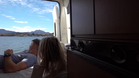 Young-couple-lying-in-back-of-campervan-and-looking-at-Lake-Wanaka,-New-Zealand