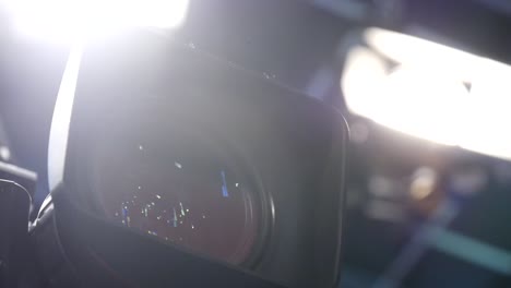 Close-up-of-a-video-camera-lens-with-bright-production-lights-on-set