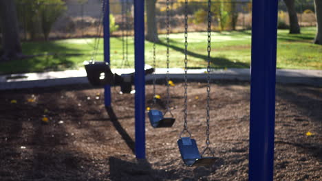 Panning-from-the-sun-and-trees-down-to-a-kids-park-playground-with-an-empty-swing-set