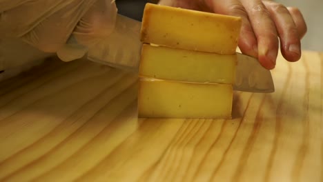 Chef-in-kitchen-restaurant-slicing-vintage-cheese-on-wooden-cutting-board---CLOSE-UP-of-hands