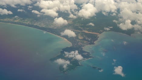 Bird's-eye-perspective-from-airplane-window-with-view-of-clouds-and-tropical-island-with-beaches