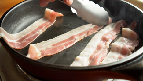 Man-Chef-cooking-for-breakfast-an-amazing-crispy-bacon,-rich-in-fat-and-colour,-sizzling-and-smoking-in-a-hot-pan